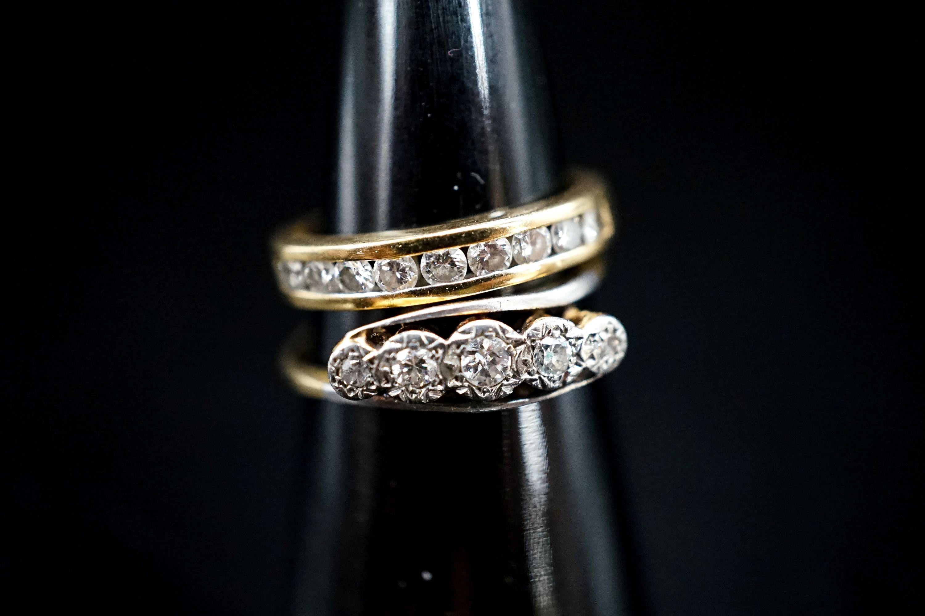 A 750 yellow metal and channel set nine stone diamond ring, size G, gross 2.6 grams and an early 20th century yellow metal and illusion set five stone diamond crossover ring, gross 2 grams.